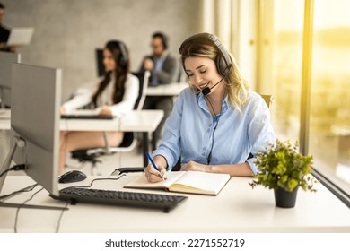 IT service support agent taking notes while talking with custumer during online phone call at help desk office at sunset.