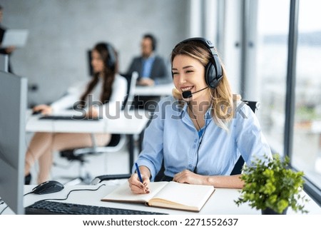 IT service support agent taking notes while talking with custumer during online phone call at help desk office.