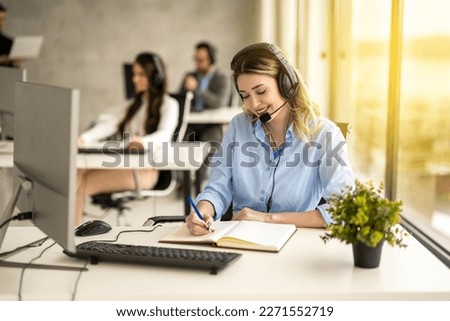 IT service support agent taking notes while talking with custumer during online phone call at help desk office at sunset.