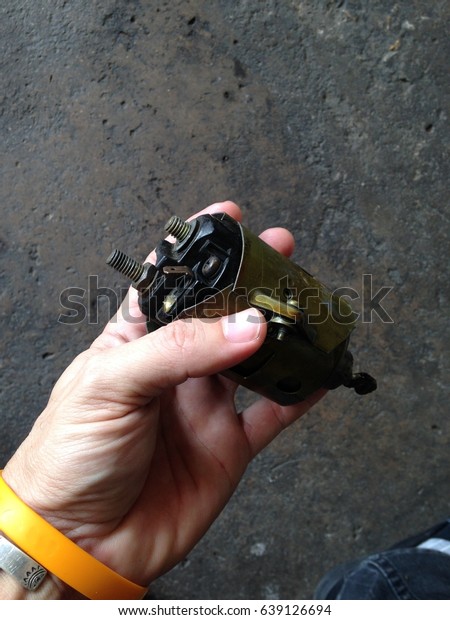 service technician hand\
holding defect worn out solenoid part disassembled from old\
gasoline starter motor engine for inspection and replace, authentic\
shot in a garage 