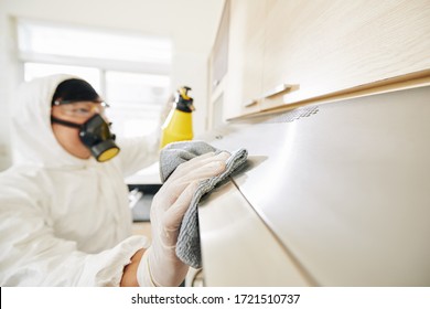 Service Worker In Hazmat Suit And Protective Mask Cleaning Furniture With Desinfecting Spray