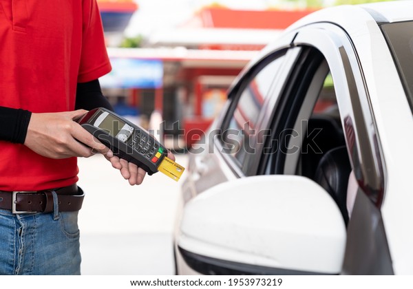 Service worker holding credit card\
reader for payment at gas station. Refuelling car and service\
payment with wireless bank payment terminal at gas\
pump