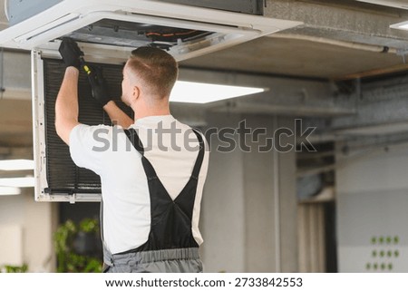 Service worker performing maintenance and checking filters on an air conditioning unit embedded in an office ceiling