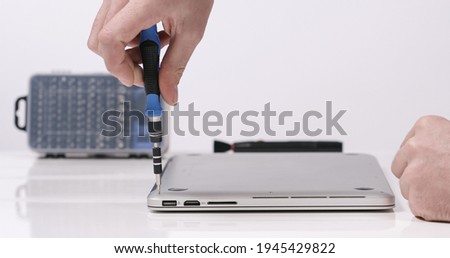 Service worker repairing laptop with magnetic screwdriver tool in white walled lab