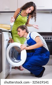Serviceman checking broken washing machine at the kitchen of young female client 