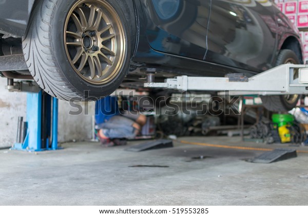 Serviceman\
checking suspension in a car at\
garage