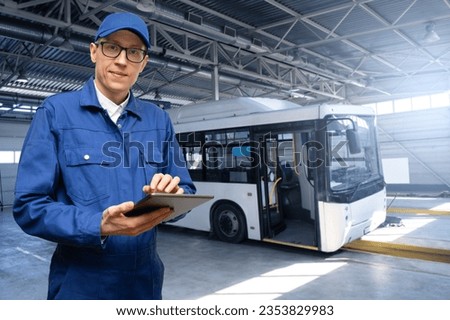 Serviceman with digital tablet on the background of the bus in the garage.