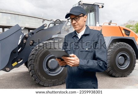 Serviceman with digital tablet on a background of the tractor.