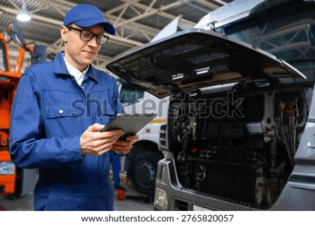 Serviceman with digital tablet on the background of the trucks in the garage	