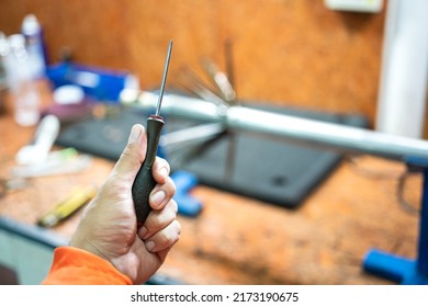 A Serviceman Is Holding Screwdriver, Preparing To Repair An Electronic Device With Workbench As Blurred Background. Industrial Working Action Photo. Selective Focus.