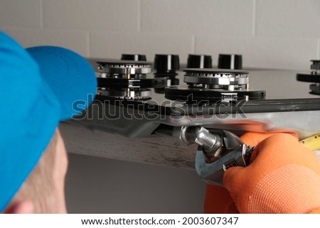 Serviceman installs  gas hob in  kitchen, connecting  gas hose