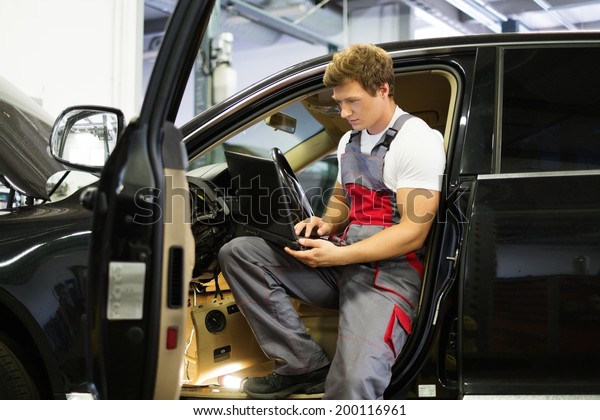 Serviceman making car diagnostics with laptop in\
a workshop