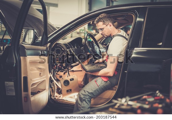 Serviceman making car diagnostics with laptop in
a workshop