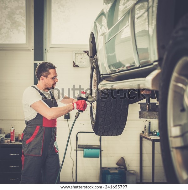 Serviceman unscrewing\
wheel in car workshop\
