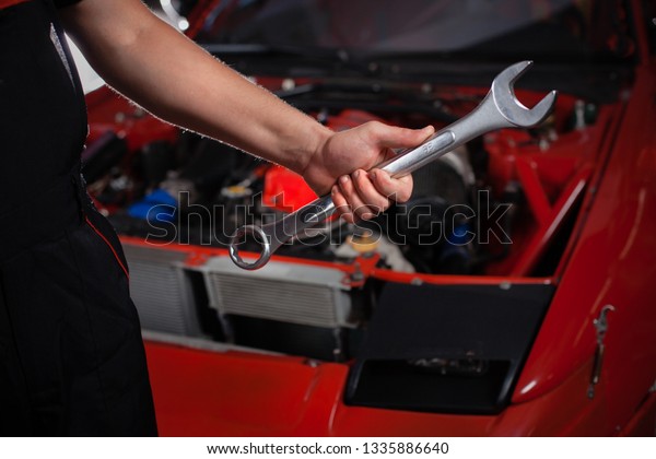 A serviceman with wrench. There is a car in the\
background. 