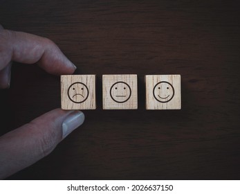 Services Rating, Ranking, Review, Feedback And Customer Satisfaction Survey Concept. Close Up Finger Choosing Not Satisfied Face Emoticon Icon On Wooden Cube Block On Dark Wood Background, Top View.