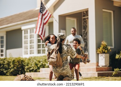 Servicewoman embracing her children after arriving home from the army. American soldier receiving a warm welcome from her husband and kids. Military woman reuniting with her family.