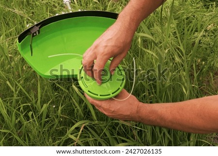 Servicing garden tools. Gardener worker attaches a reel to a mower in a meadow with grass. Close-up of a man's hand taking apart a lawn mower to replace parts. Replacing the coil in a lawn mower