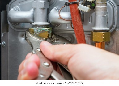 Servicing A Heating Home System.Technician With Wrench Repairs Leaked Hot Water Pipe In Gas Heater. Close-up, Selective Focus.