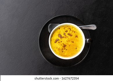 Serving of aromatic and healthy turmeric black coffee against dark table