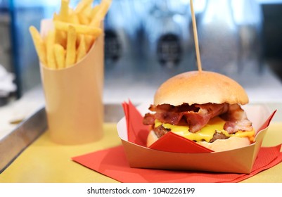 Serving a crunchy hamburger with melted cheese and bacon on a disposable cardboard plate on a tray with a side order of French fries