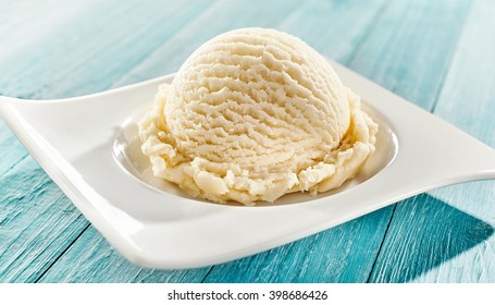 Serving of delicious frozen creamy vanilla ice cream on a modern rectangular plate outdoors on a blue rustic picnic table for summer dessert