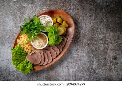 Serving a dish from the restaurant menu. Sliced beef tongue with pickles, cabbage, sauces and herbs on a plate against a gray stone table, a delicious appetizer