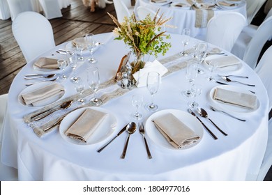 Serving a festive table, placing plates on the table, a Banquet table with a white tablecloth, preparing the dining table for the holiday, Cutlery is arranged according to etiquette. flowers