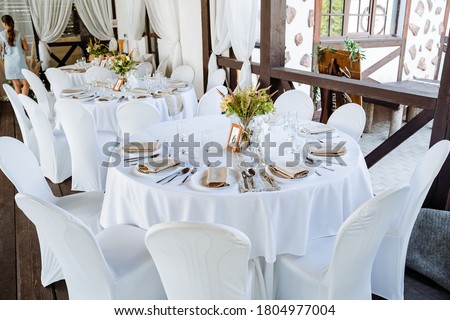 Serving a festive table, placing plates on the table, a Banquet table with a white tablecloth, preparing the dining table for the holiday, Cutlery is arranged according to etiquette. flowers