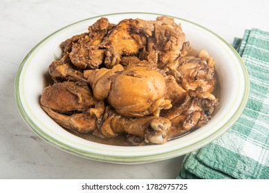 A serving of Filipino-style chicken adobo dish in a bowl with green napkin set on a marble tabletop.