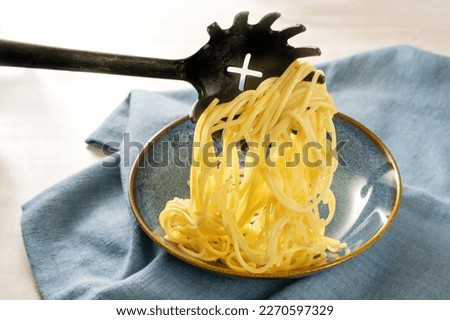 Serving fresh pasta, spaghetti are filled onto a blue plate with a special spoon, napkin on a light table, copy space, selected focus, narrow depth of field
