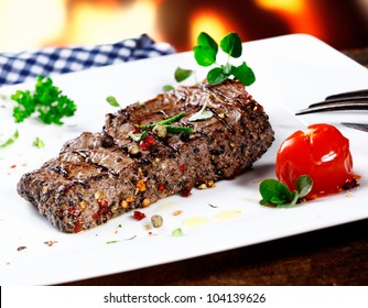 Serving of grilled beef steak coated in hot peppercorns and garnished with fresh herbs and a tomato