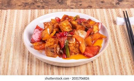 Serving of hot sweet and sour tofu with onions and peppers in a plate with chopsticks, close-up