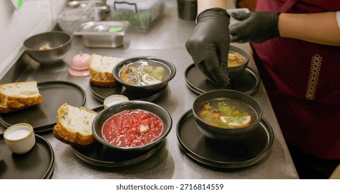 Serving meal. Kitchen process. Cafeteria chef garnishing hot dish with chopped fresh herbs. Hands adding aroma greens in soup borsch.