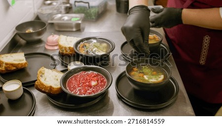 Serving meal. Kitchen process. Cafeteria chef garnishing hot dish with chopped fresh herbs. Hands adding aroma greens in soup borsch.