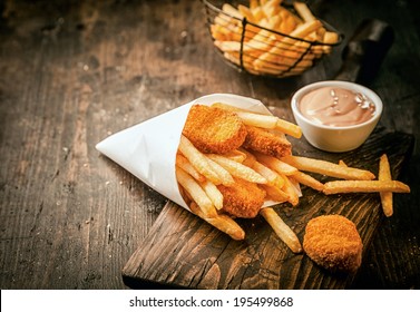 Serving in a paper cone of takeaway crumbed fried fish nuggets with potato chips and a small bowl of sauce or dip on a rustic wooden table with copyspace - Powered by Shutterstock