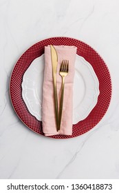Serving plate for holiday with red and white plate, pink napkin and golden fork and knife on marble background. Concept of table setting on holiday, New Year, Christmas, Purim, Independence Day 