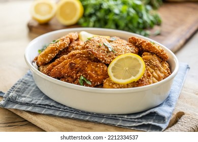 Serving of schnitzels in a white shallow bowl with slice of lemon.