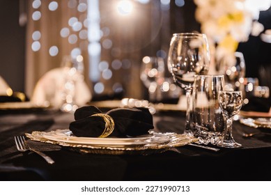 Serving, setting table. Plate decorated linen black napkin and silverware cutlery, glasses. Side view. Closeup. Wedding set up, dinner table reception. Birthday, baptism, event. Luxury golden decor. - Powered by Shutterstock