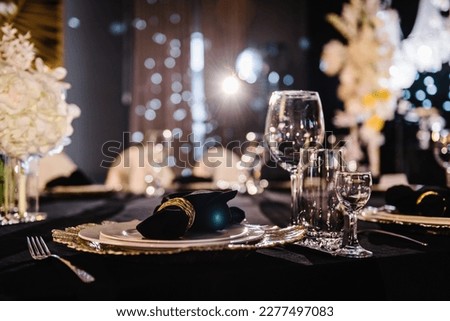 Serving, setting table. Plate decorated linen black napkin and silverware cutlery, glasses. Side view. Closeup. Wedding set up, dinner table reception. Birthday, baptism, event. Luxury golden decor.