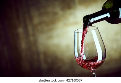 Serving a single glass of red wine from a bottle with a close up view of the neck of the bottle and glass over a wide angle abstract brown background with copy space
