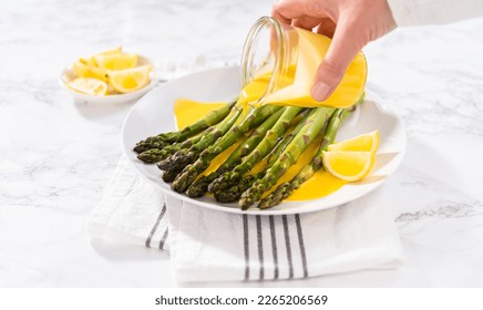 Serving steamed asparagus with homemade hollandaise sauce with lemon wedges on a white plate.