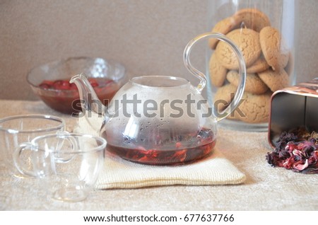 Serving table for breakfast, red tea in teapot. tea leaves, hibiscus and two glass cups for tea