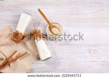 Sesame milk in bottles, sesame seeds in a jar on a wooden background. A healthy vegetarian and vegan drink, a plant-based milk substitute. Zero waste.