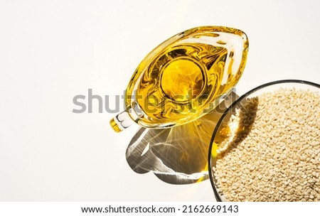 Sesame seed and oil in glass bowl, close up on white background.