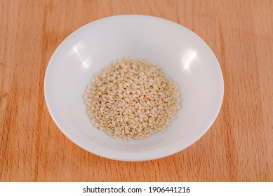 Sesame Seeds in a white bowl on a wooden chopping board background