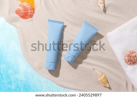 Set against a fresh sea background with sand, starfish, seashells, white towel and two vibrant blue cosmetic tubes, perfect for seasonal cosmetic advertising. Mockup.