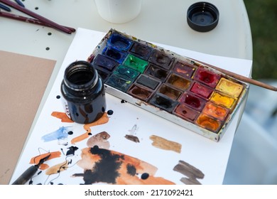 Set Artist. Watercolor Paints, Brushes And Feathers Under The Ink. A Jar Of Black Paint. Brushstrokes Watercolors On White Sheet