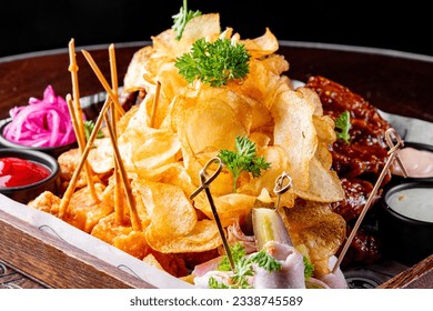 Set of assorted beer snacks and sauces served in a wooden box on dark concrete background. Potato chips, nachos, french fries, rye bread croutons, chicken wings, fried cheese - Powered by Shutterstock