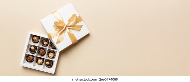 A set of assorted chocolates in a paper box with a satin purple ribbon on a bright background. A place for design. Flat layout. Celebratory concept. Copy space